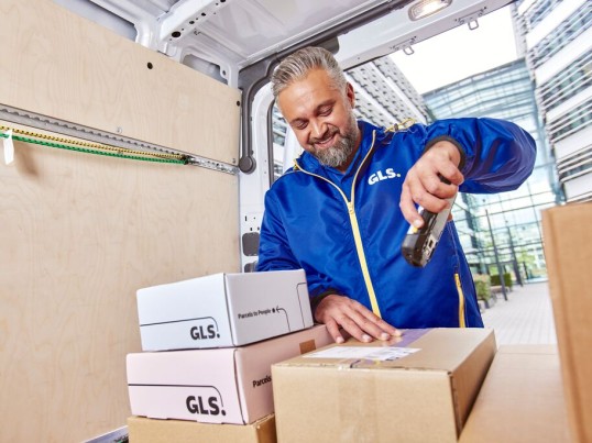  Un conductor de GLS escanea un paquete en la parte trasera de una furgoneta de reparto.