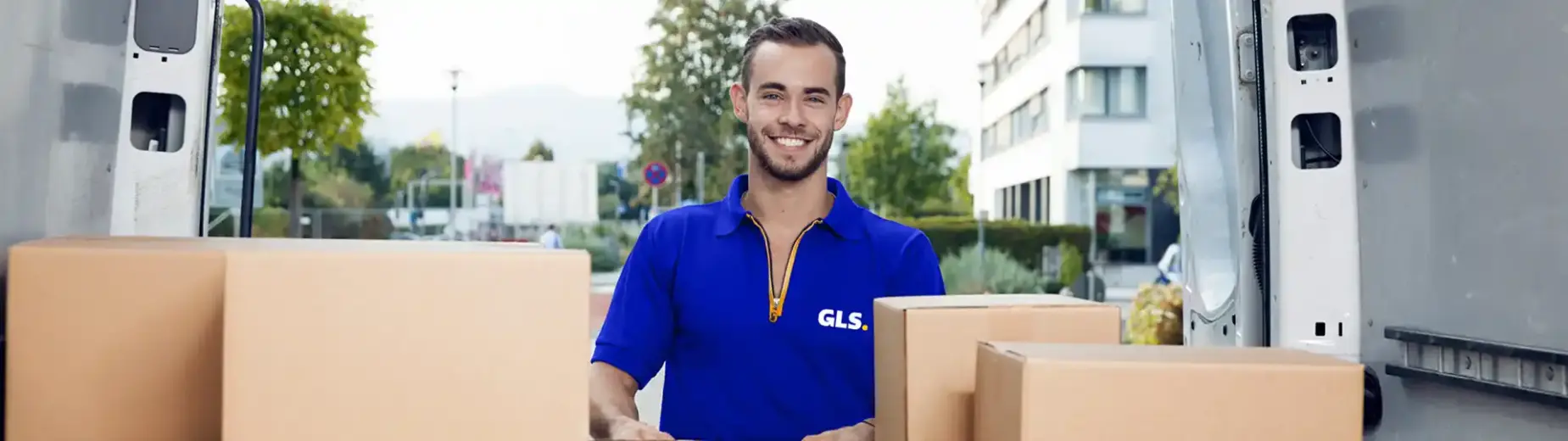Livreur GLS avec colis devant un véhicule de livraison GLS lors d’une distribution de colis en zone urbaine.