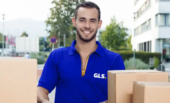 Livreur GLS avec colis devant un véhicule de livraison GLS lors d’une distribution de colis en zone urbaine.