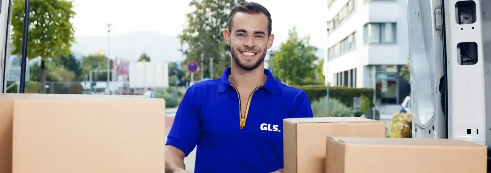 Livreur GLS avec colis devant un véhicule de livraison GLS lors d’une distribution de colis en zone urbaine.