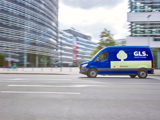 GLS driver smiling while holding a parcel in front of an open delivery van
