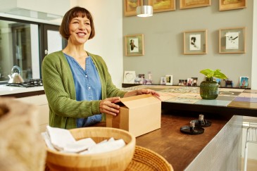 femeie în bucătărie zâmbind în timp ce ține un colet 