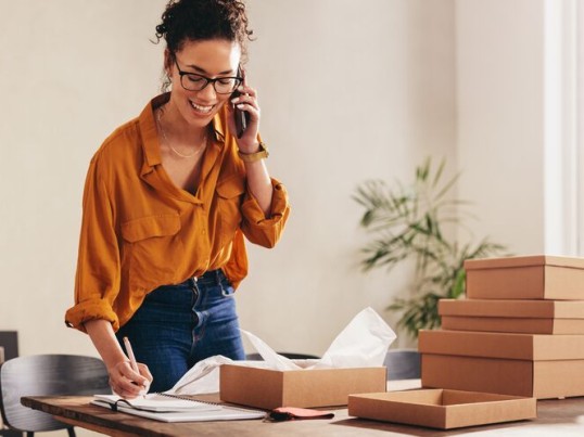 Žena telefonuje a zároveň balí balíky