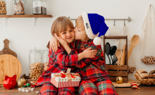Malý chlapec dáva pusu malému dievčatku, obaja majú vianočné pyžamá.